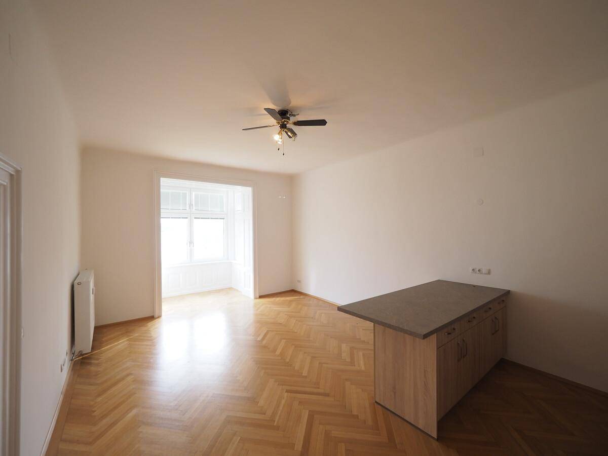 Offener Wohnbereich mit Fischgrätparkett, Deckenventilator und einer Kücheninsel.
