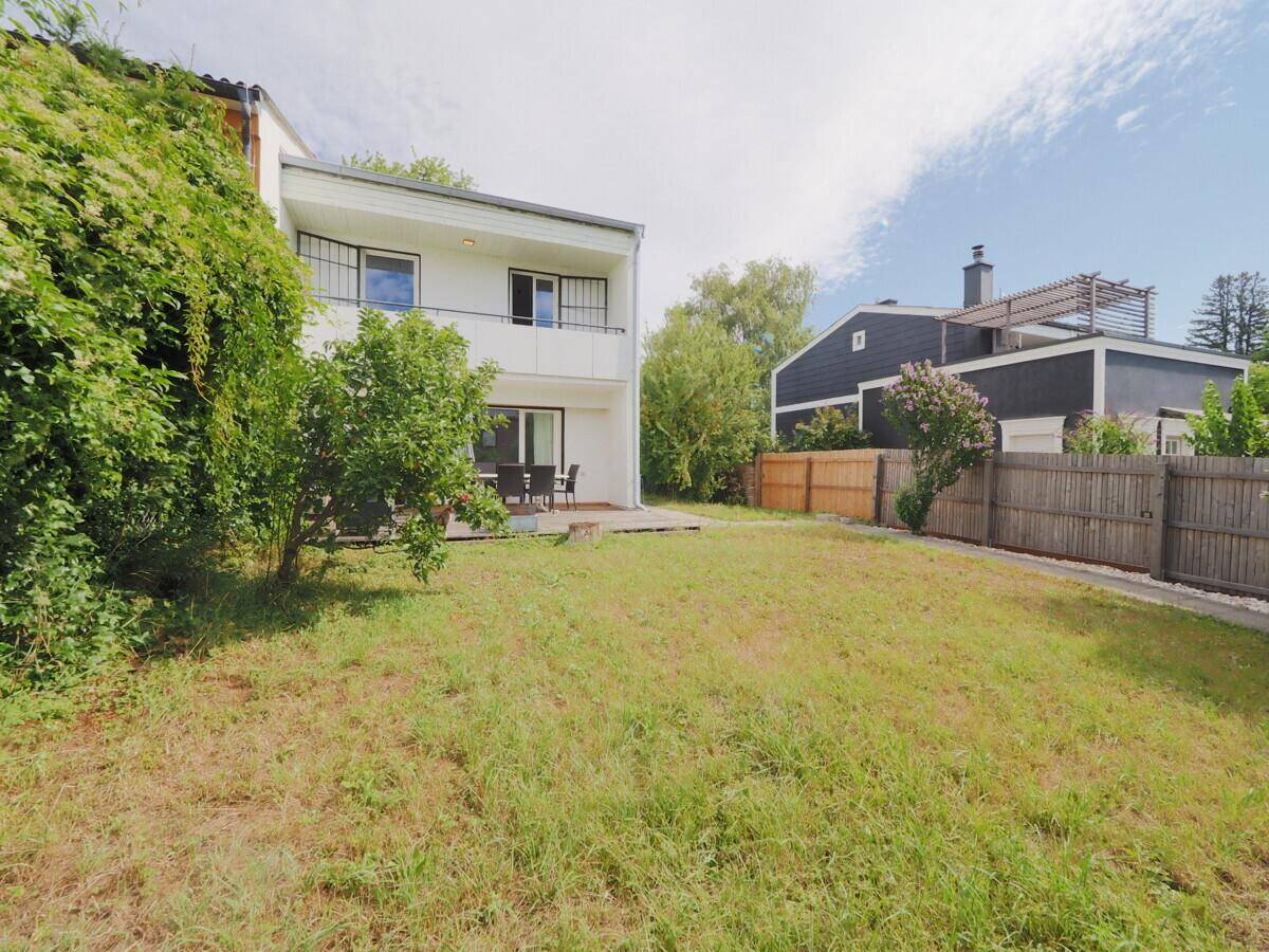 Rückansicht des weißen Hauses mit Balkon, Terrasse und großem Garten.