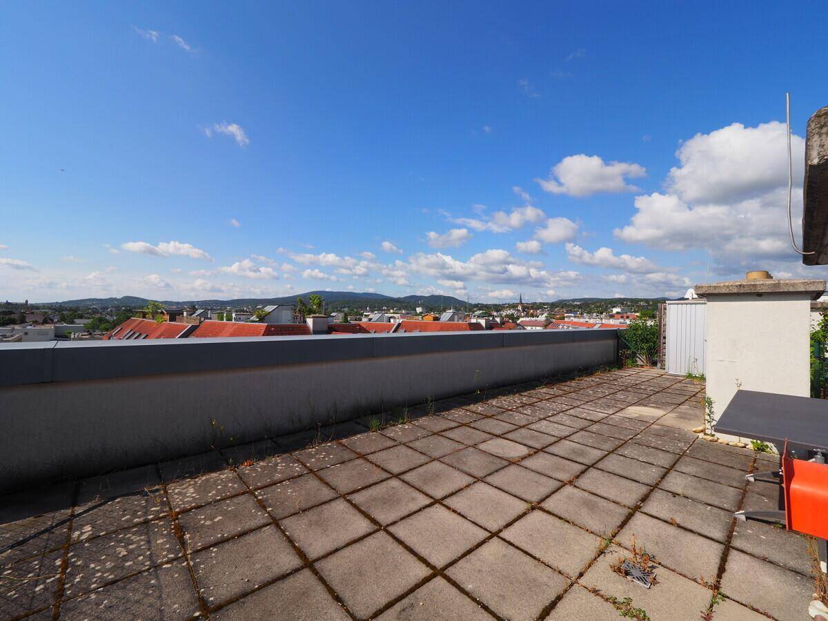 Große Dachterrasse mit Fliesenboden und weitem Blick über die Stadt und die umliegende Landschaft.