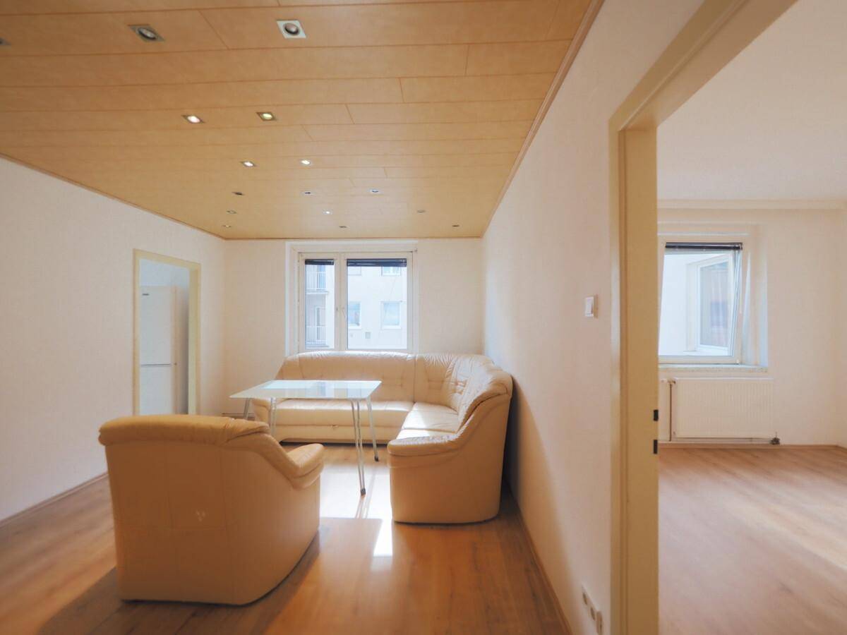 Gemütliches Wohnzimmer mit Holzdecke, Einbaustrahlern und Blick in einen angrenzenden Raum mit Heizkörper.