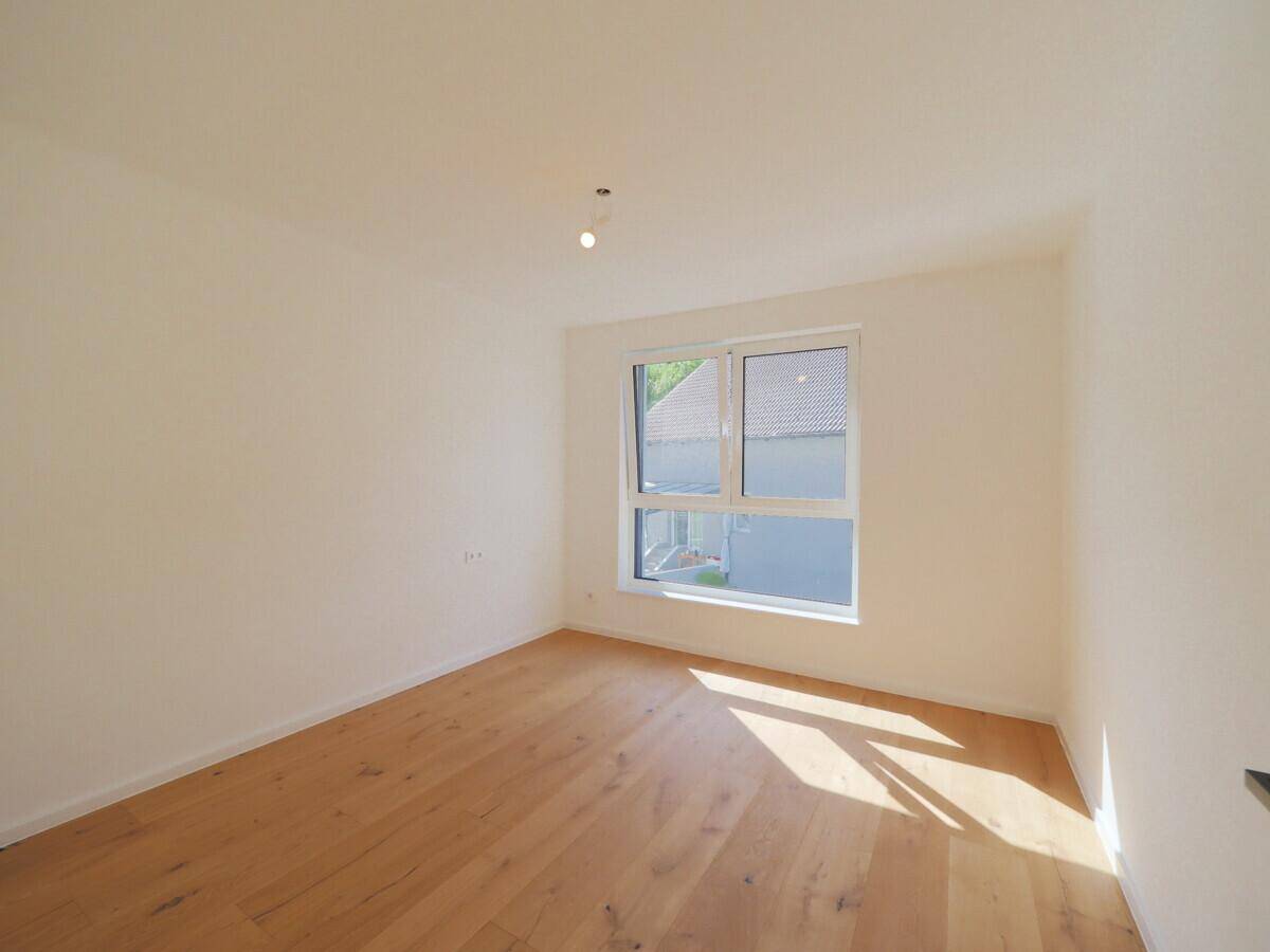 Geräumiges Schlafzimmer mit hellem Parkettboden und Fenster mit Blick ins Grüne.