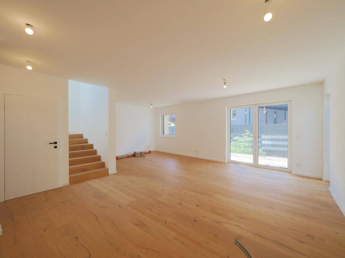 Großzügiges Wohnzimmer mit hellem Eichenparkett, Zugang zur Terrasse und Treppe zum Obergeschoss.