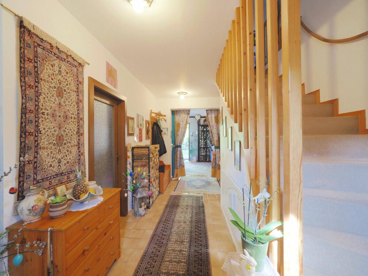 Heller Flur mit Holztreppe, Teppichläufer und traditionellen Dekorationselementen.