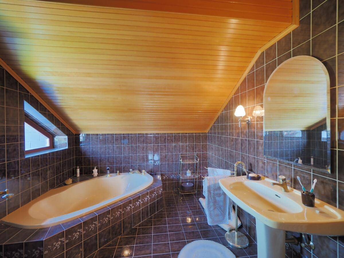 Badezimmer im Dachgeschoss mit Badewanne, Waschbecken und dunklen Fliesen.