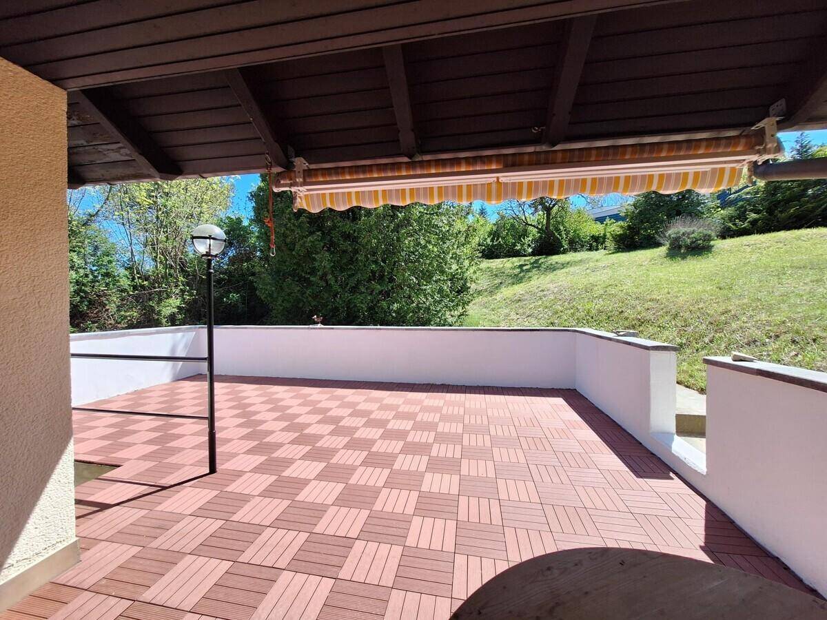 Überdachte Terrasse mit gemustertem Boden und Blick auf eine grüne Hügellandschaft.