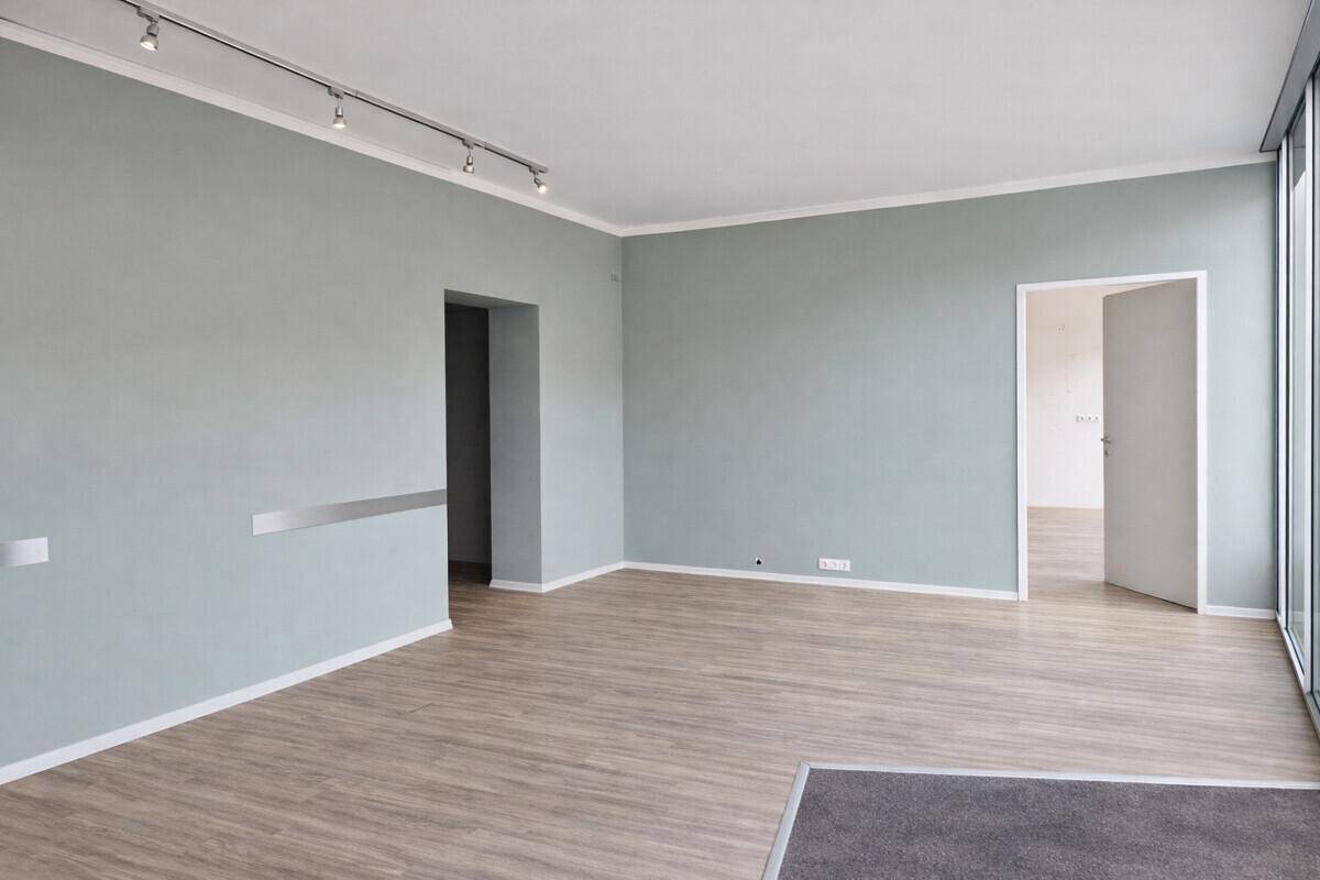 Geräumiger Büroraum mit großen Fenstern, die viel Tageslicht hereinlassen, und einem modernen Laminatboden.