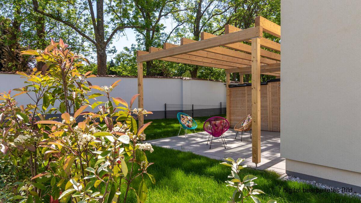 Gemütliche Terrasse unter einer Holzpergola mit bunten Gartenstühlen, umgeben von blühenden Pflanzen.