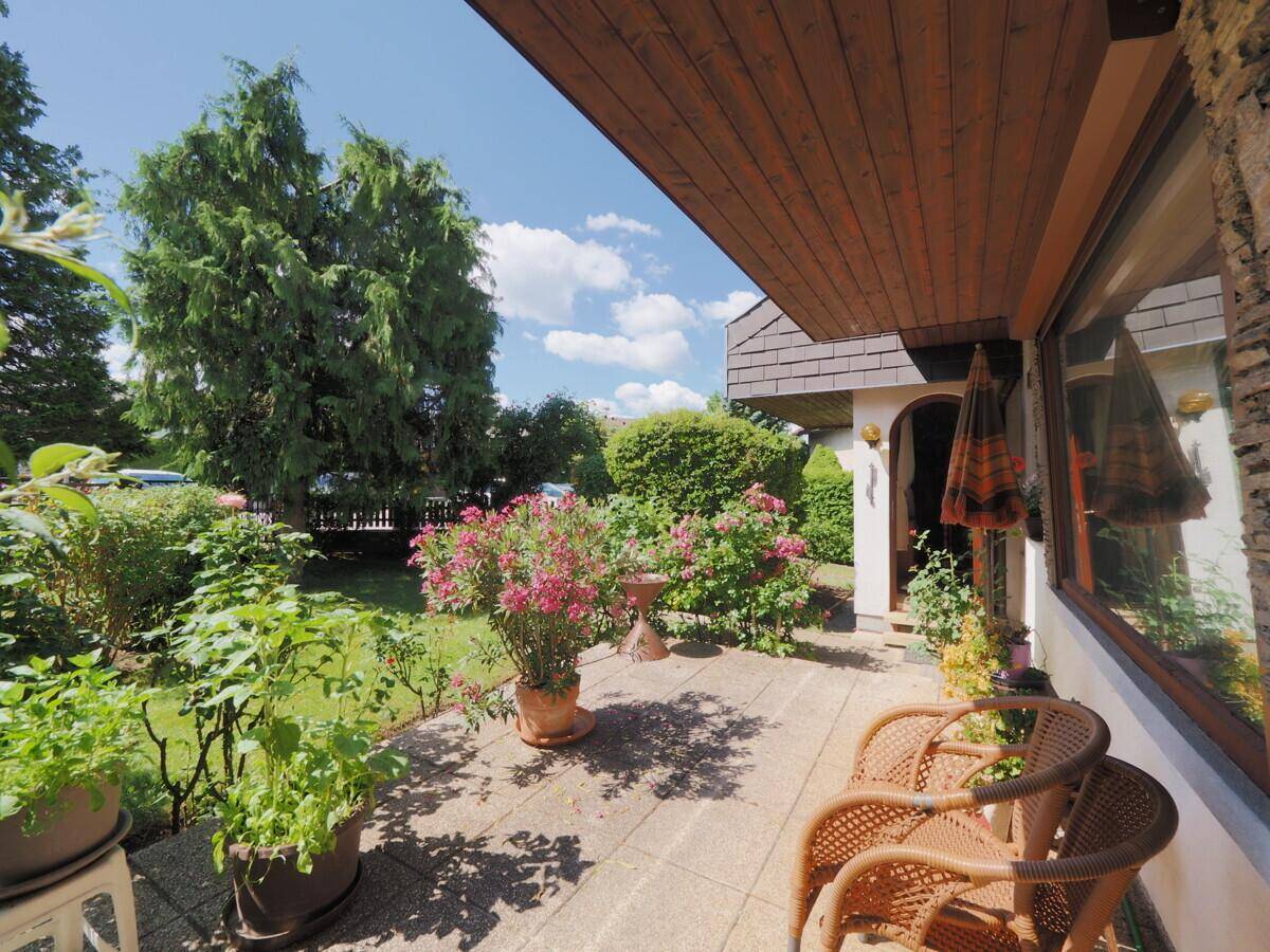 Sonniger Terrassenbereich mit Sitzgelegenheiten, Blumen und Blick in den Garten.