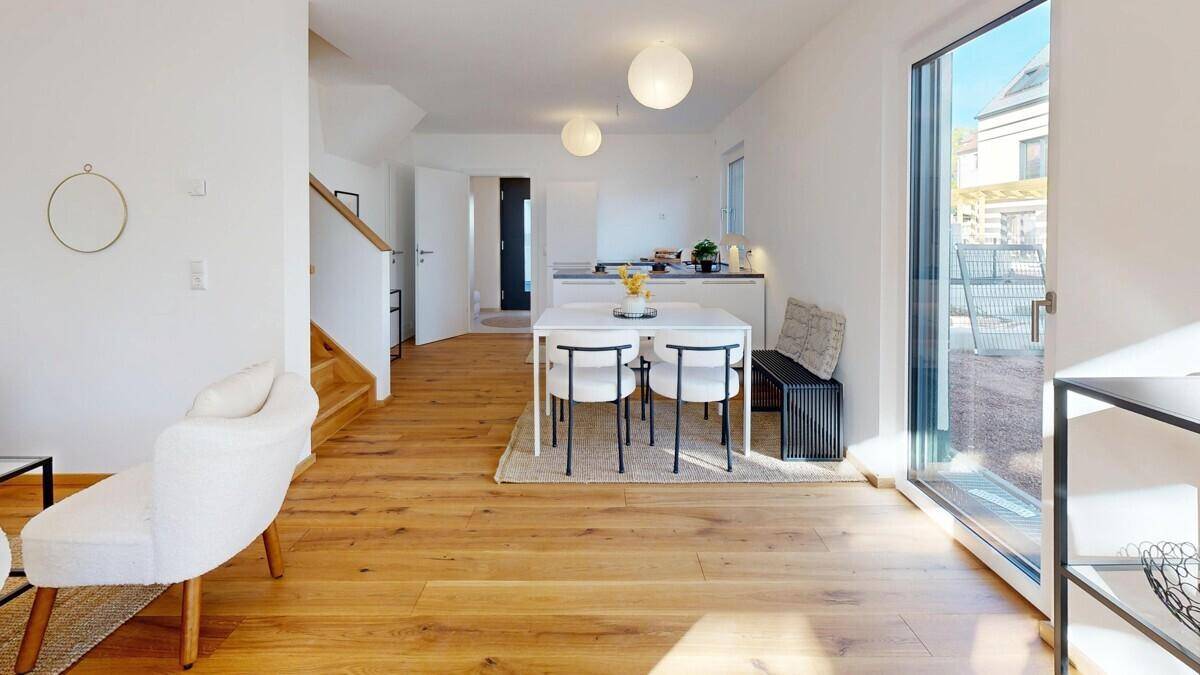 Offener Wohn- und Essbereich mit Holzboden, moderner Einrichtung und Zugang nach draußen.