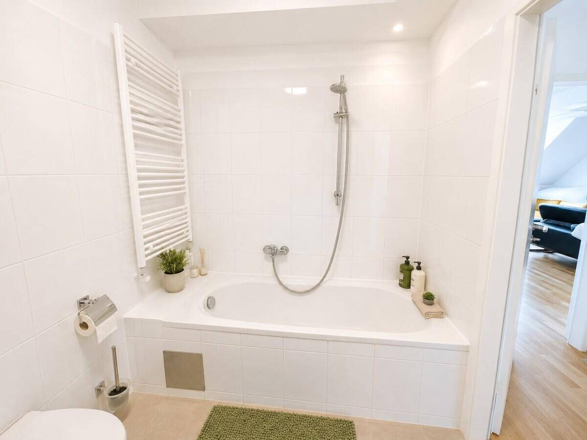 Helles Badezimmer mit Badewanne inklusive Duschfunktion und beheiztem Handtuchhalter.