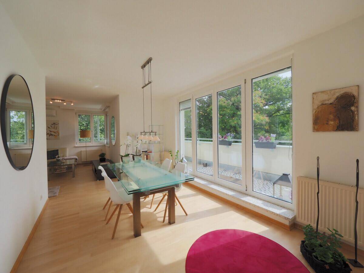 Heller Essbereich mit Holzboden, großem Esstisch und Zugang zum Balkon mit Grünblick.