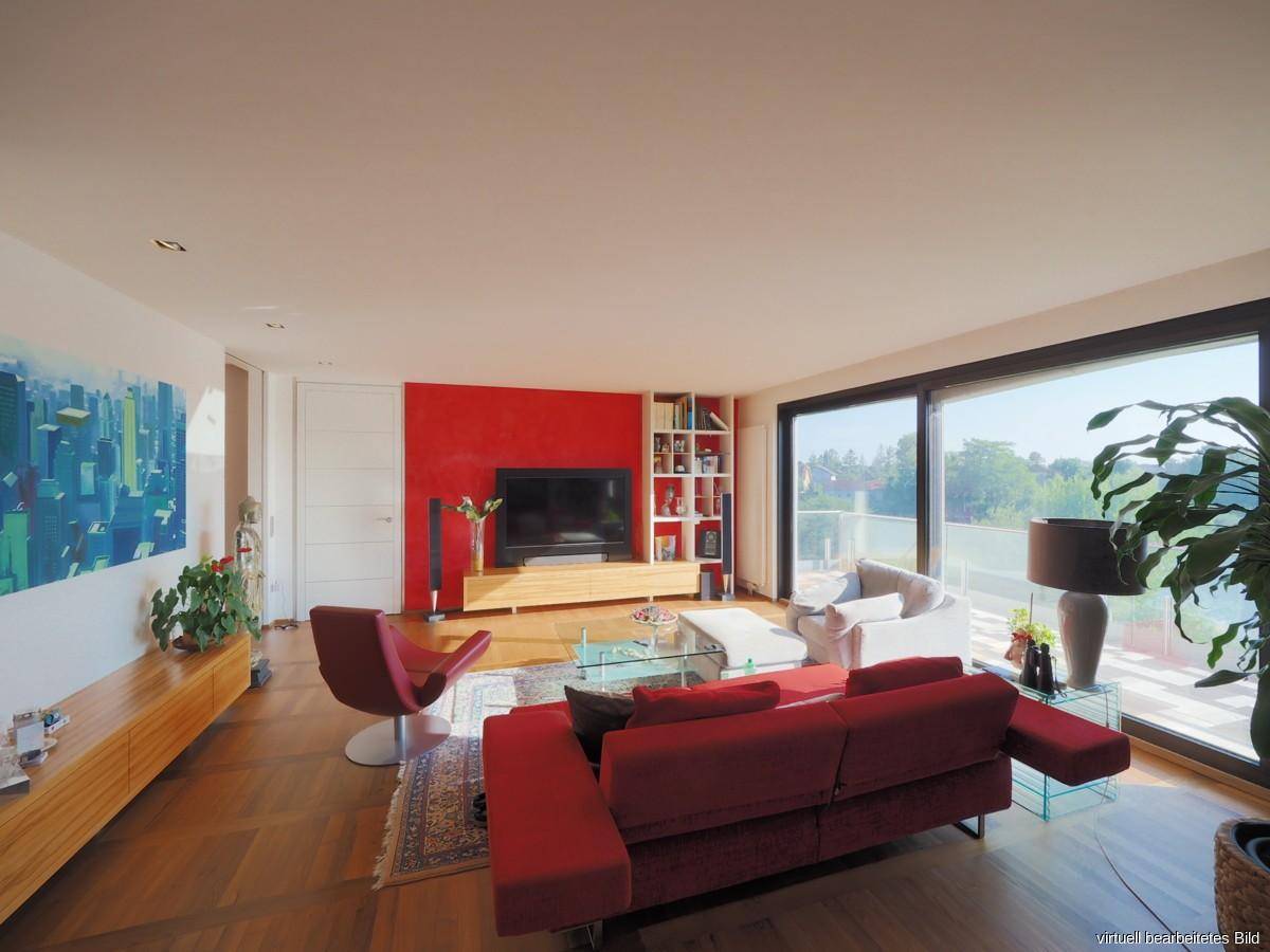 Helles Wohnzimmer mit großen Fensterfronten, roter Akzentwand und Blick ins Grüne.