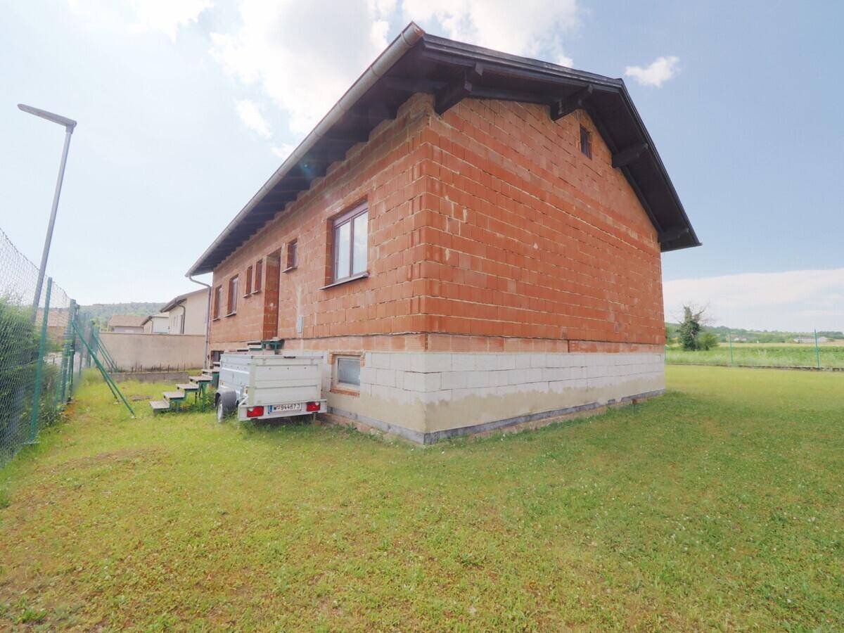 Seitenansicht des Rohbaus mit unverputzten Ziegelwänden und angrenzendem Grundstück.