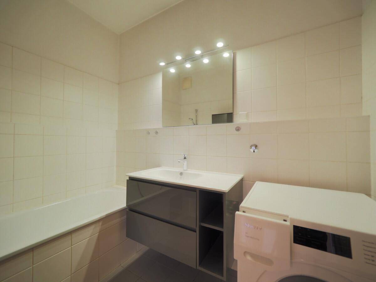 Helles Badezimmer mit Badewanne, Waschbecken und Waschmaschine, funktional und gefliest.