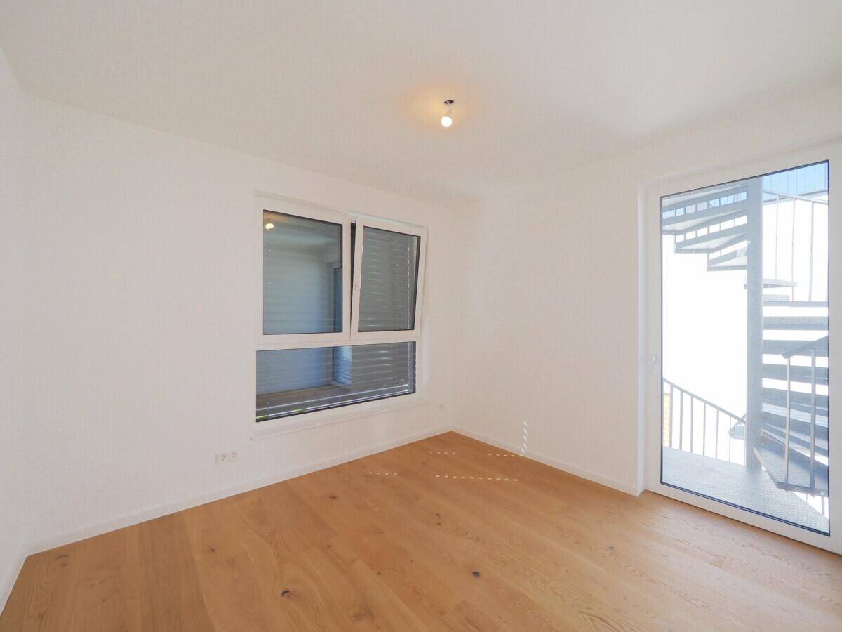 Helles Zimmer mit Holzboden und Zugang zur Außentreppe.