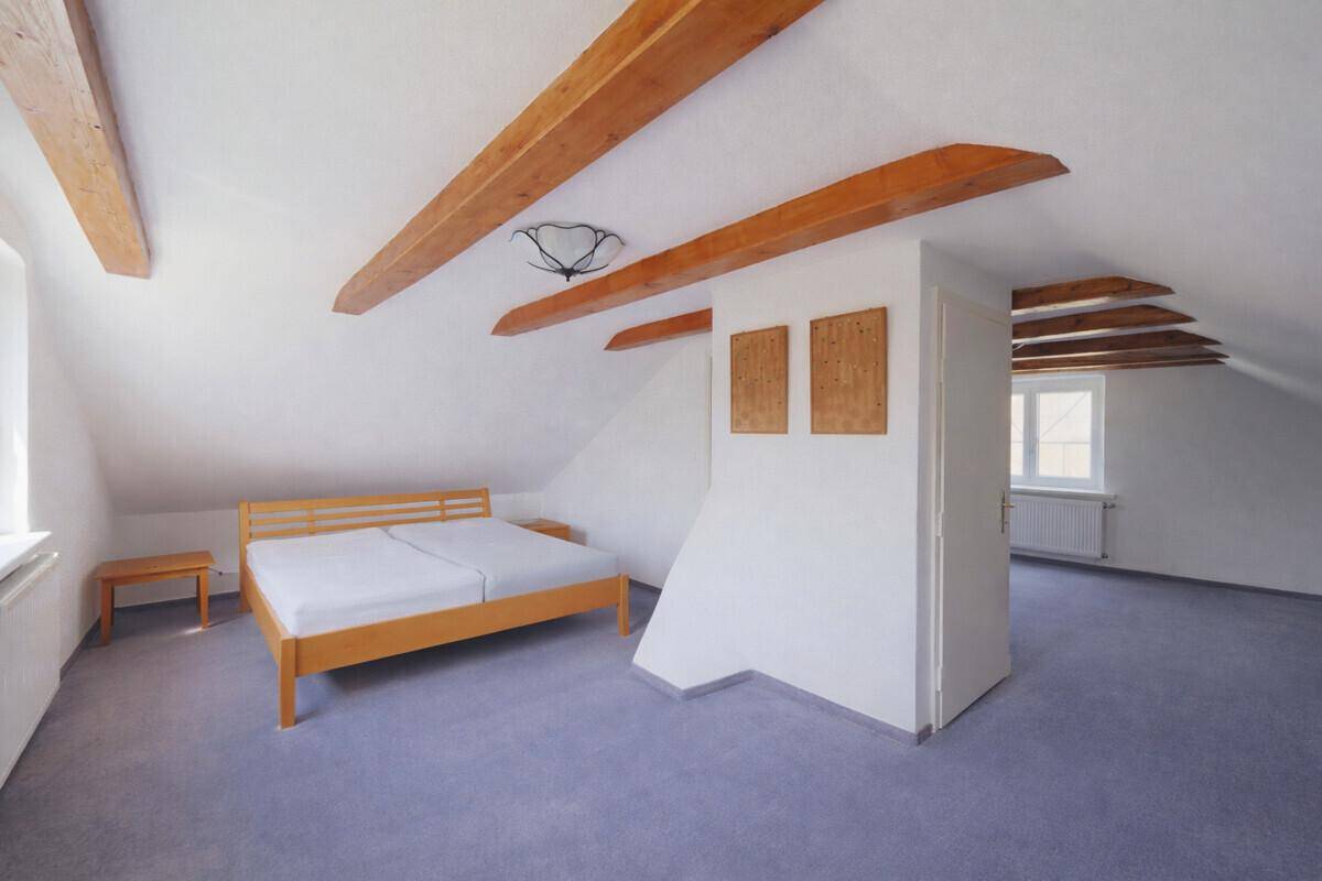 Geräumiges Dachzimmer mit sichtbaren Holzbalken, Teppichboden und Doppelbett.