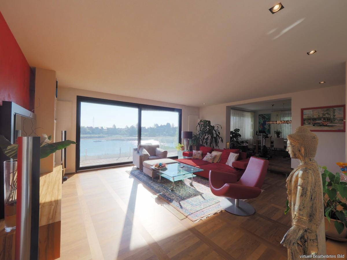 Lichtdurchflutetes Wohnzimmer mit Seeblick, rotem Sofa und Holzboden.