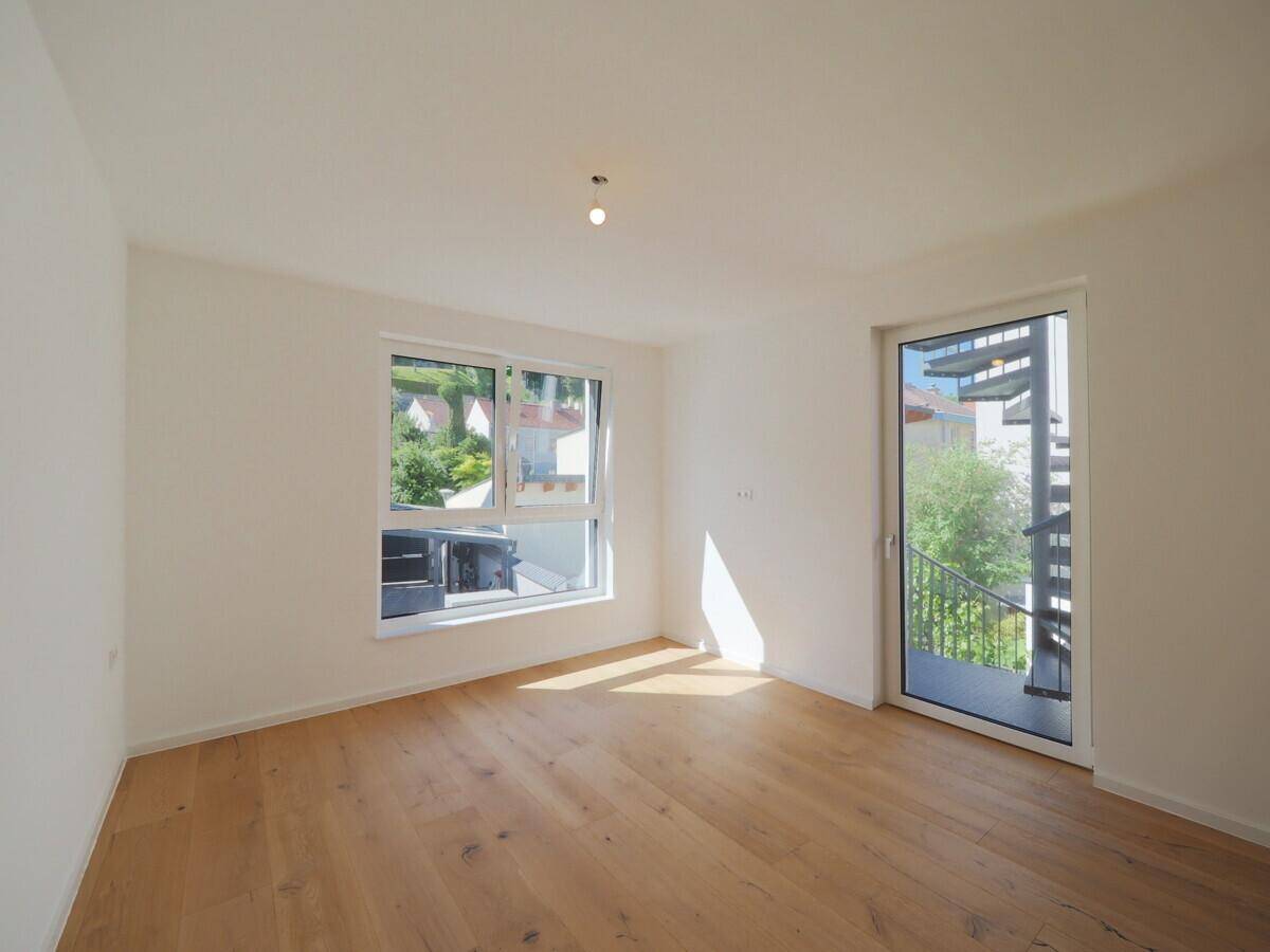 Geräumiges Zimmer mit Holzboden, weißen Wänden und Zugang zu einer Außentreppe.