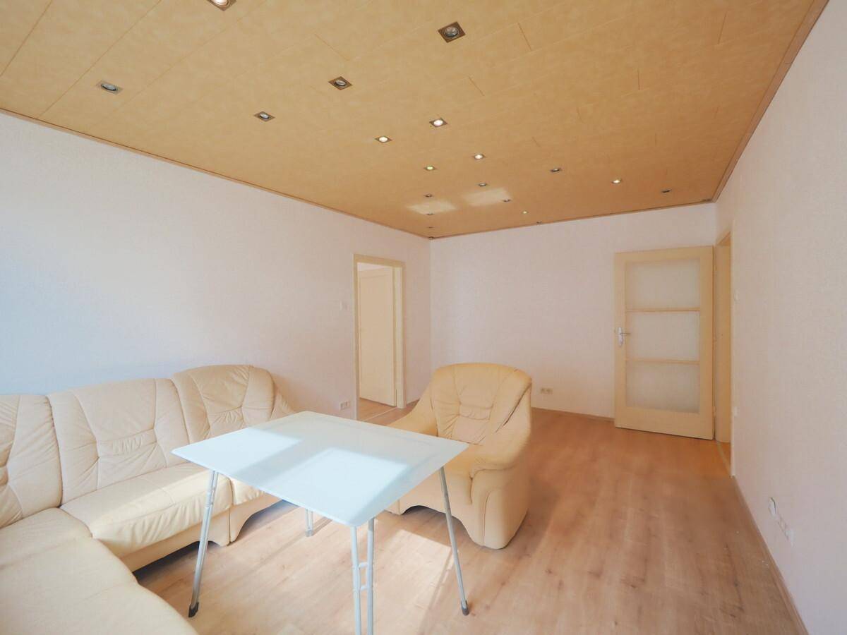 Wohnzimmer mit beiger Sitzecke, Holzdeckenpaneelen und einer Tür mit Glaseinsätzen.