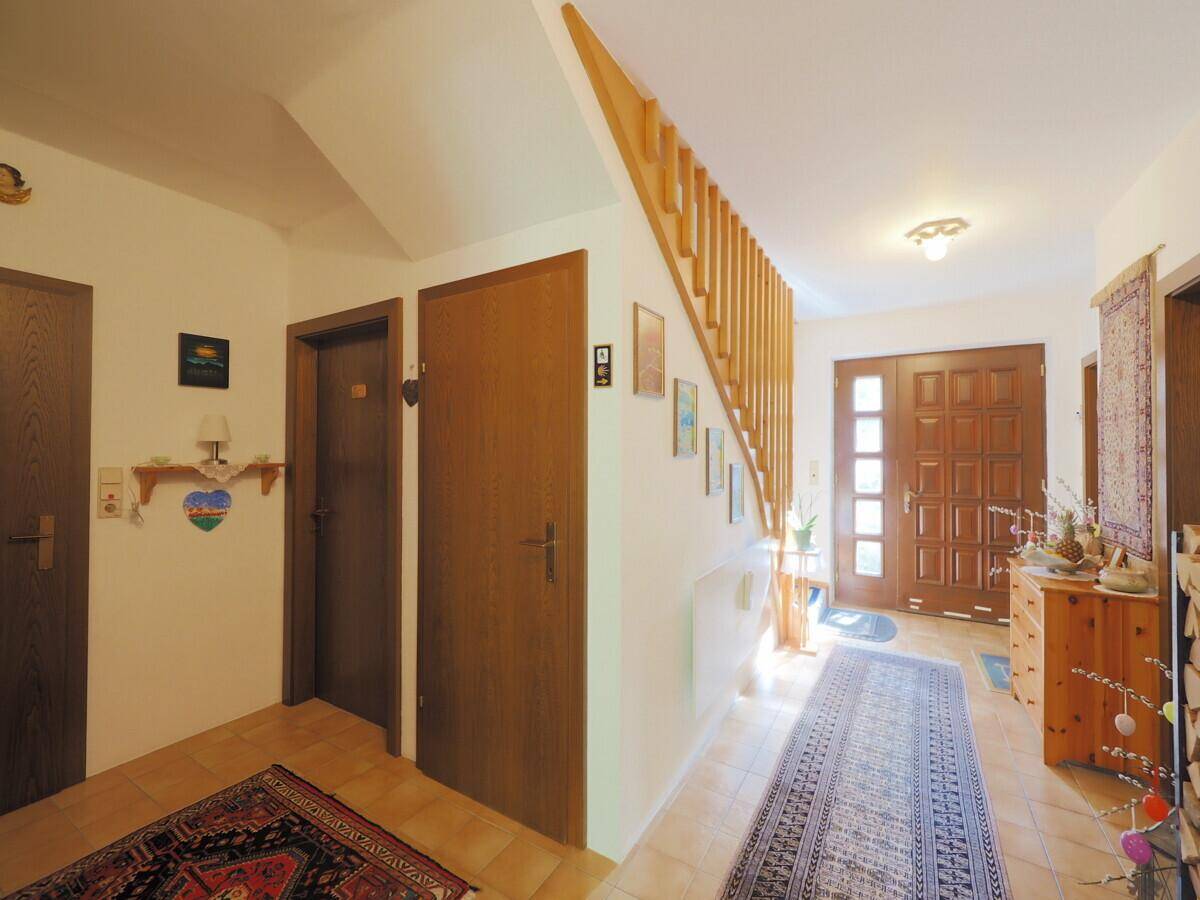 Eingangsbereich mit Holztüren, gefliestem Boden und einer Holztreppe zum Obergeschoss.