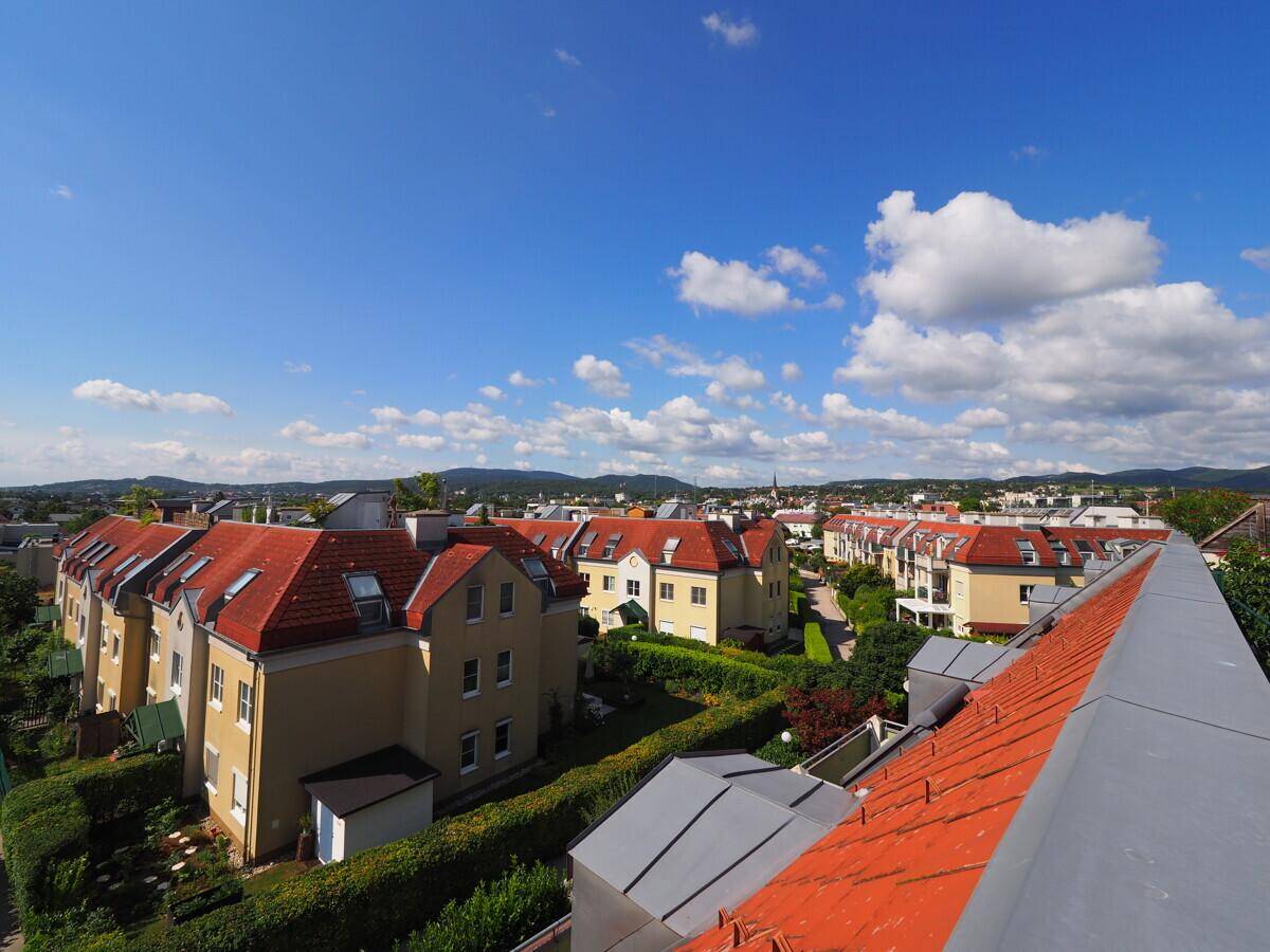 Weitläufige Ansicht einer Wohngegend mit roten Dächern und viel Grün unter strahlendem Himmel.