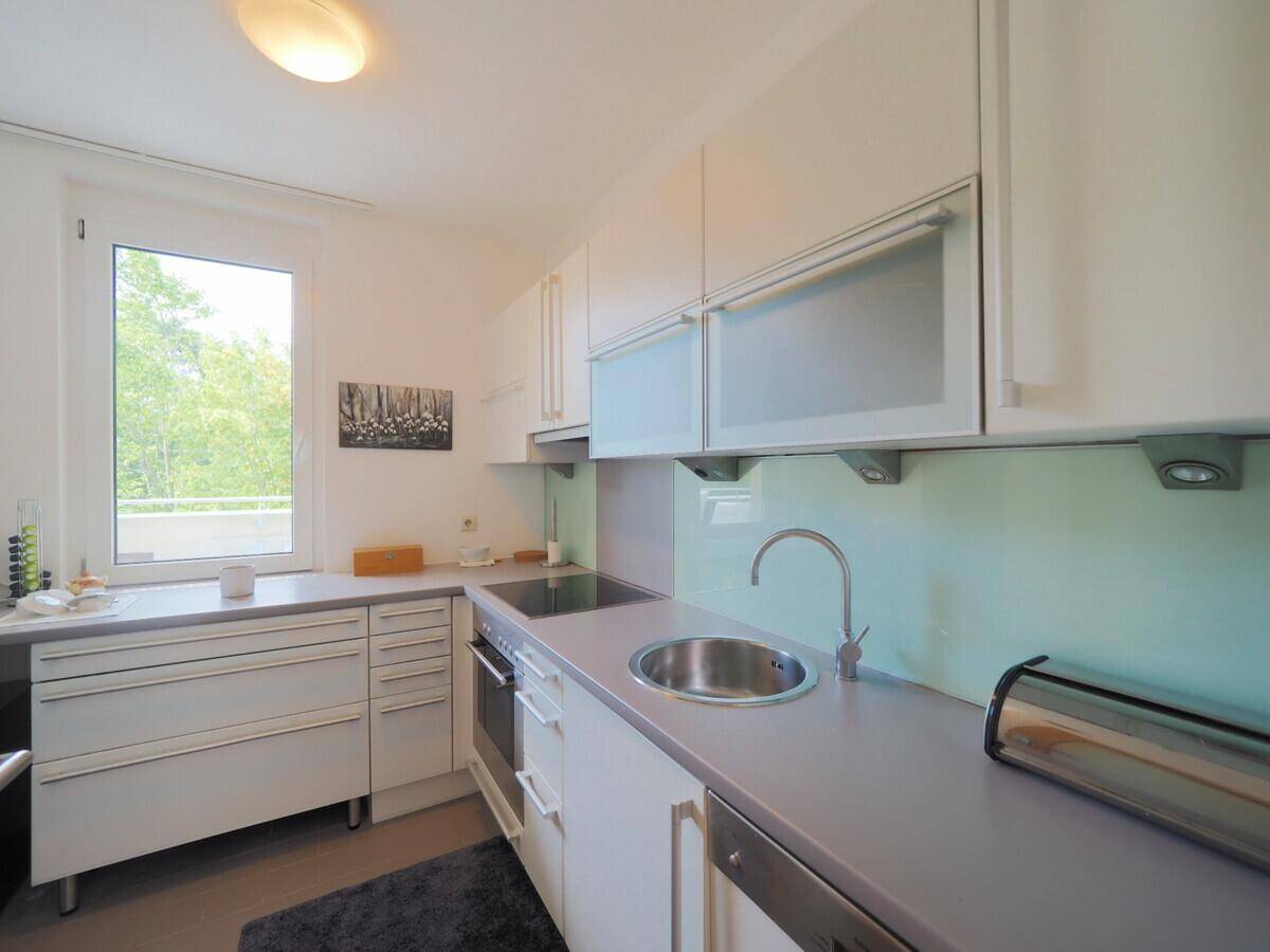 Moderne Einbauküche mit weißen Schränken, integrierten Geräten und Fenster mit Grünblick.