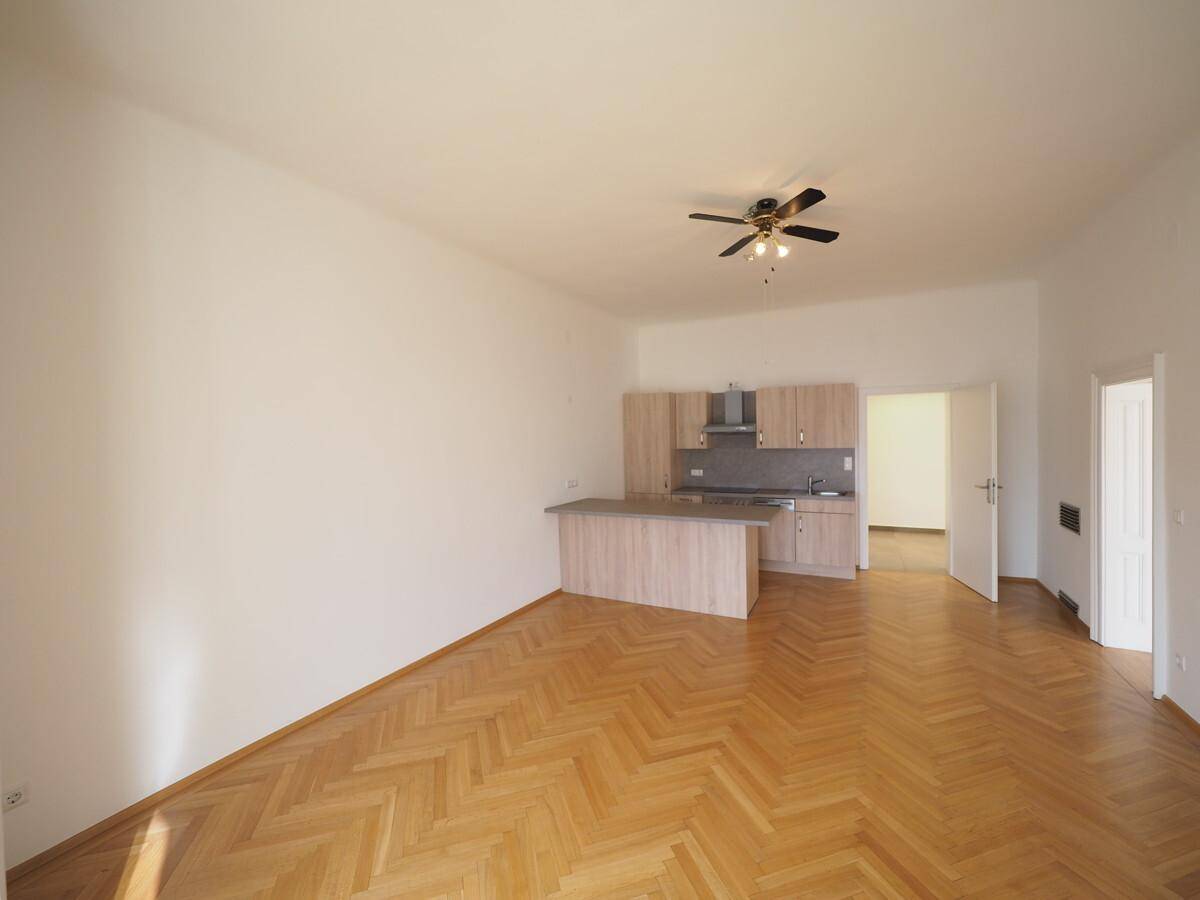 Geräumiger offener Wohnbereich mit Holzboden, Deckenventilator und moderner Küchenzeile.