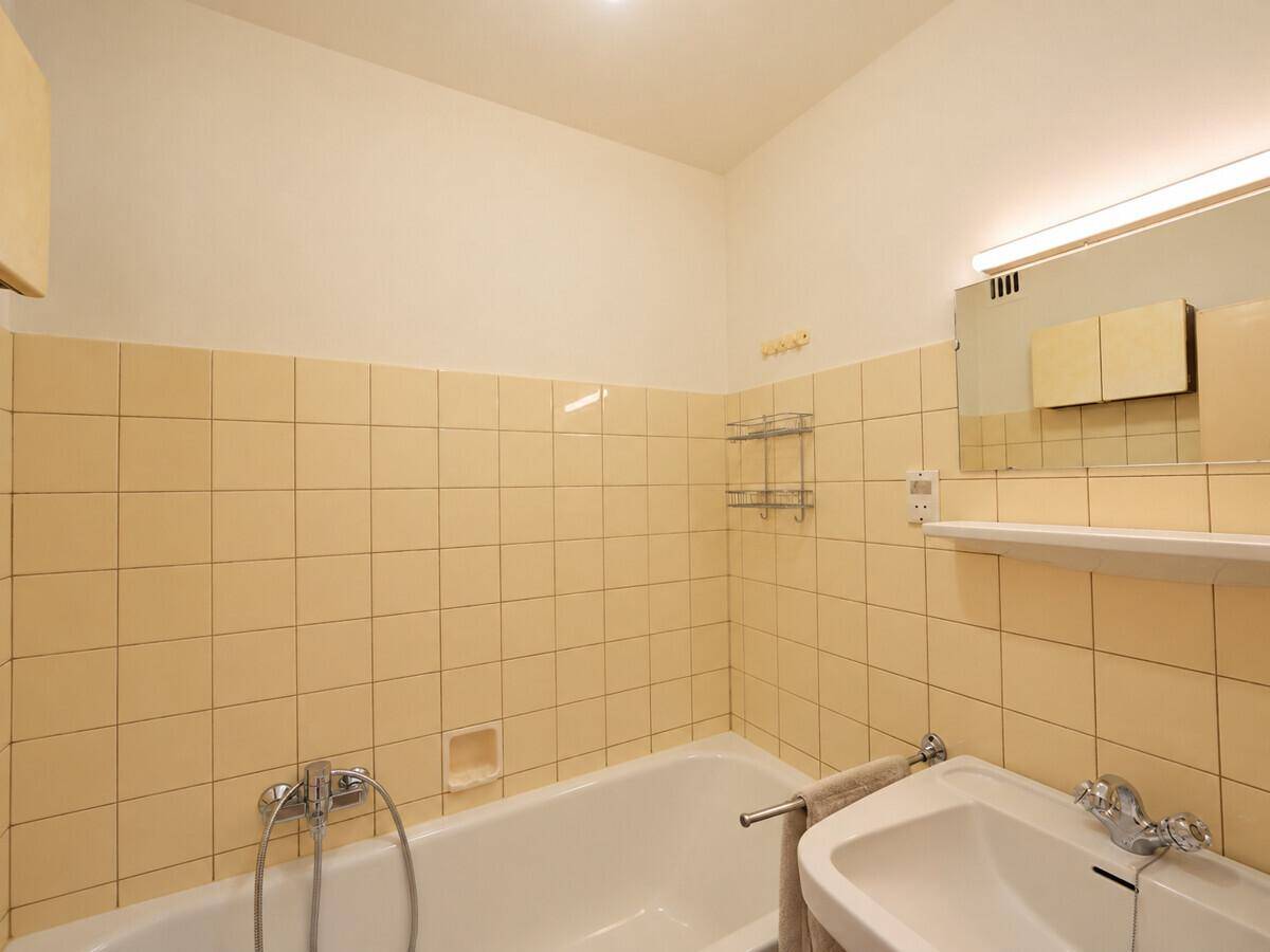 Badezimmer mit gelben Fliesen, Badewanne und Waschbecken in funktionalem Zustand.