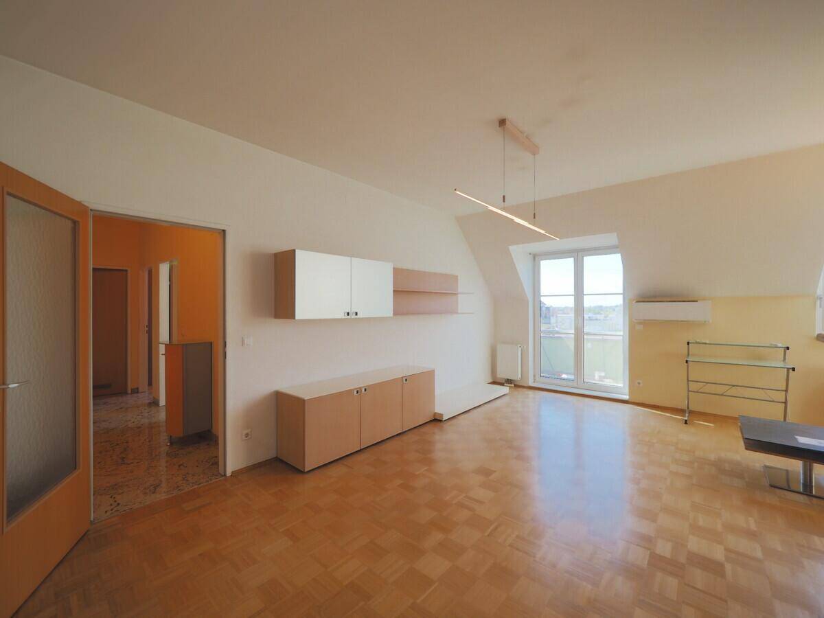 Heller Wohnbereich mit Parkettboden, Dachschräge und Zugang zu einem großen Fenster mit Ausblick.