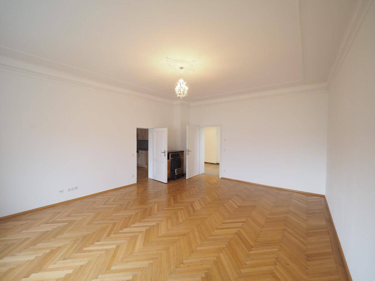 Helles Wohnzimmer mit klassischem Fischgrätparkett, hohen Decken und eleganter Deckenleuchte.
