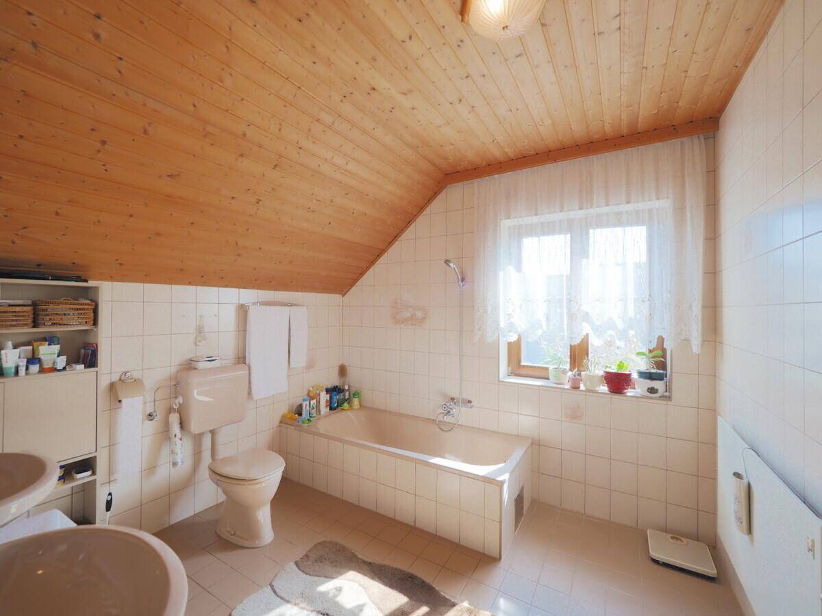 Geräumiges Badezimmer mit Dachschräge, Badewanne, WC und Holzdecke.