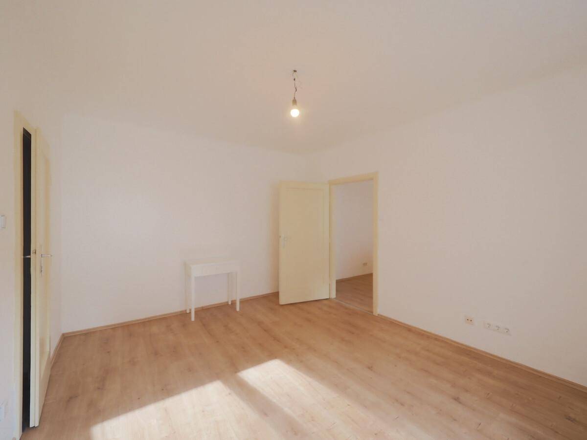 Heller, leerer Raum mit Laminatboden und zwei Türen, bereit zur individuellen Gestaltung.