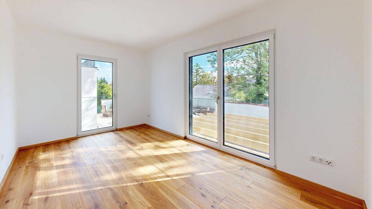 Leerer Raum mit Holzboden und großen Fenstern, die viel Tageslicht hereinlassen.