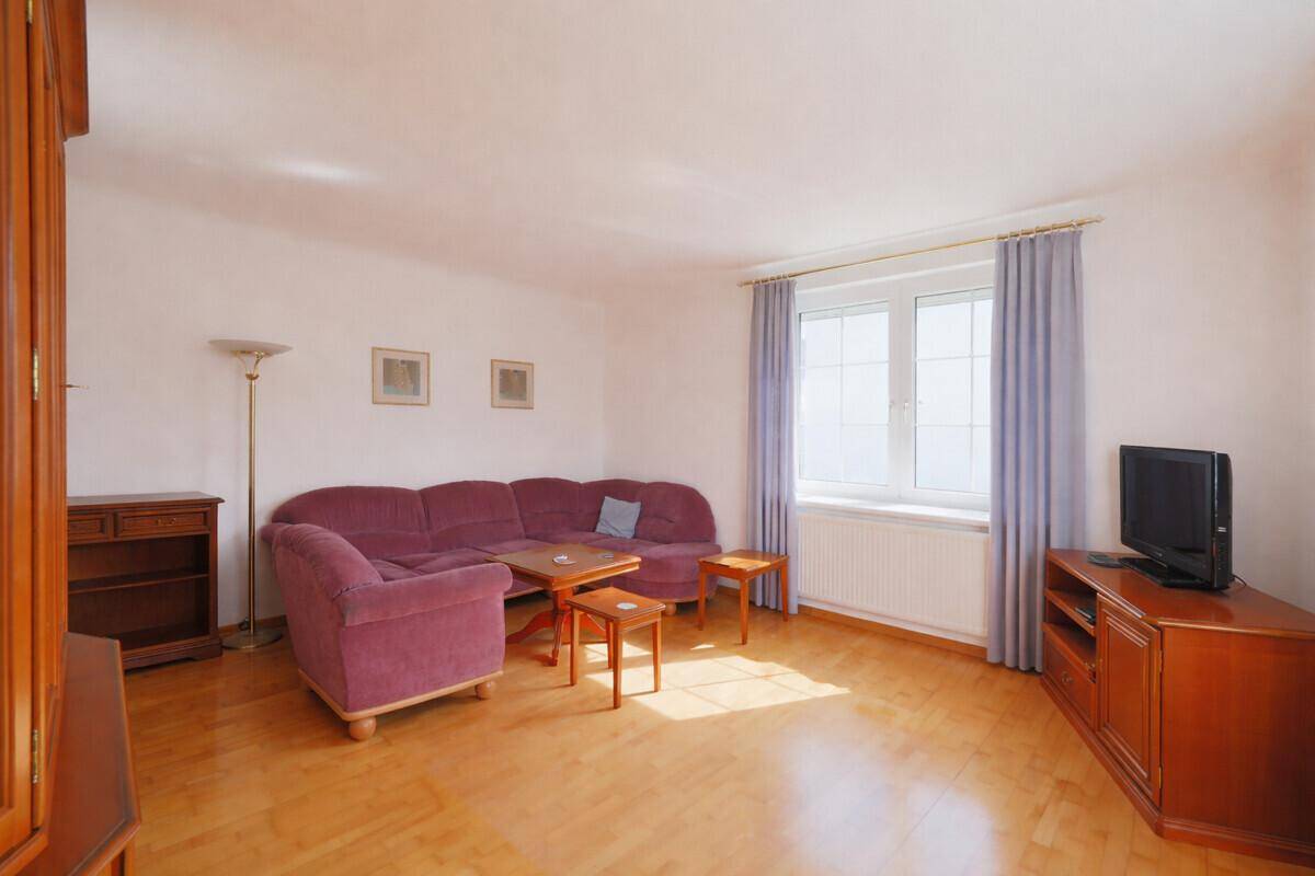 Gemütliches Wohnzimmer mit Parkettboden, lila Sofa und großem Fenster für viel Tageslicht.