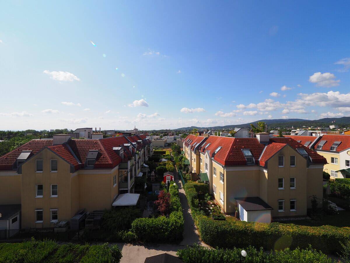 Luftaufnahme einer Wohnsiedlung mit Reihenhäusern und grünen Gärten unter blauem Himmel.