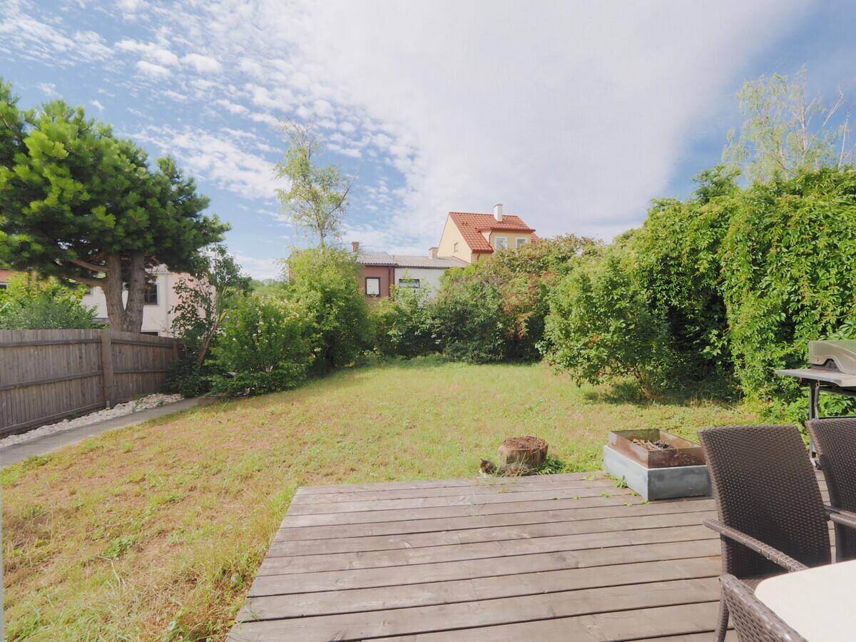 Garten mit Holzterrasse, Rasenfläche und Grillbereich, umgeben von Hecken.