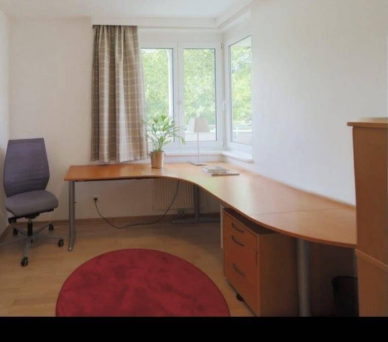 Helles Arbeitszimmer mit Eckschreibtisch, Holzboden und großen Fenstern mit Grünblick.