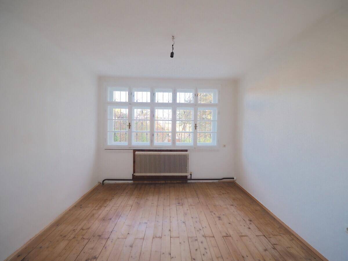 Helles Zimmer mit Dielenboden, großem Fenster und Heizkörper, ideal für Schlaf- oder Wohnbereich.