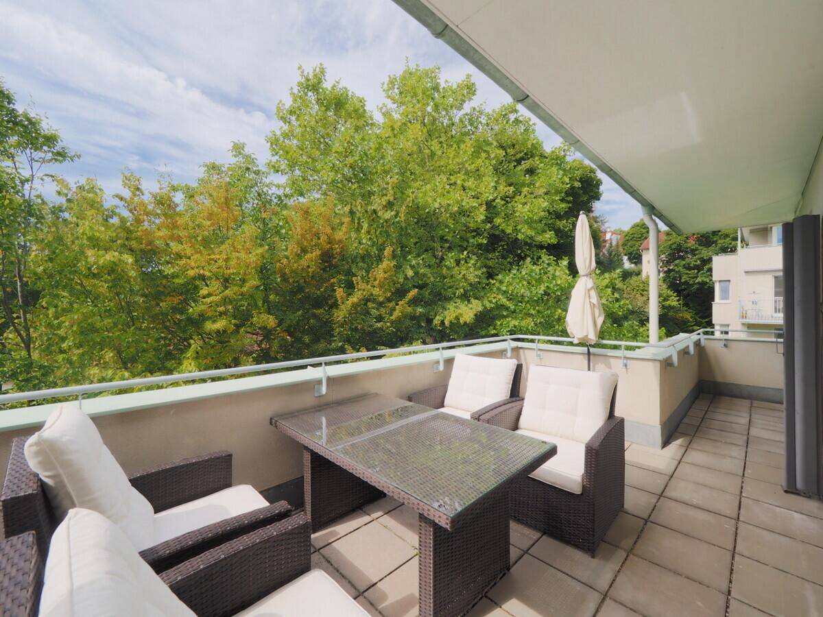 Geräumiger Balkon mit Sitzgelegenheiten und Markise, umgeben von üppigem Grün.