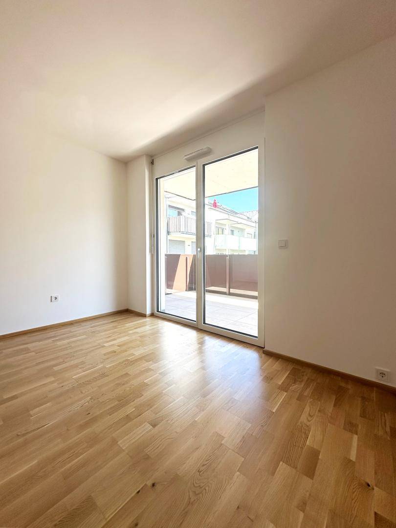 Heller Raum mit Parkettboden und Zugang zu einem Außenbereich durch eine große Glastür.