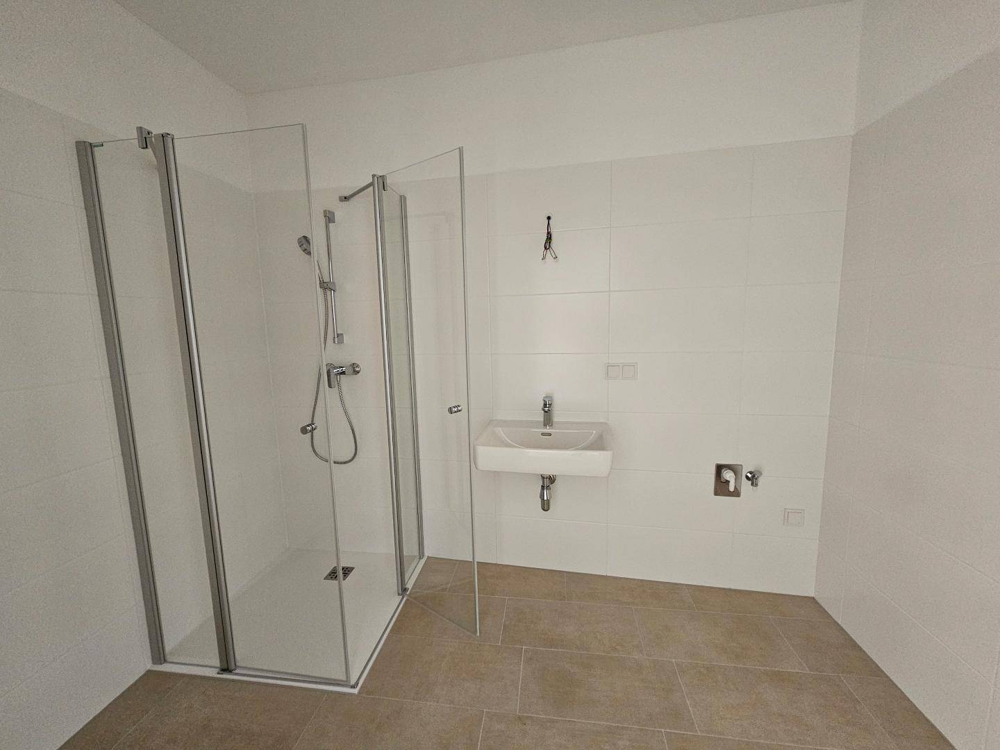 Modernes Badezimmer mit Duschkabine, weißem Waschbecken und hellen Fliesen.