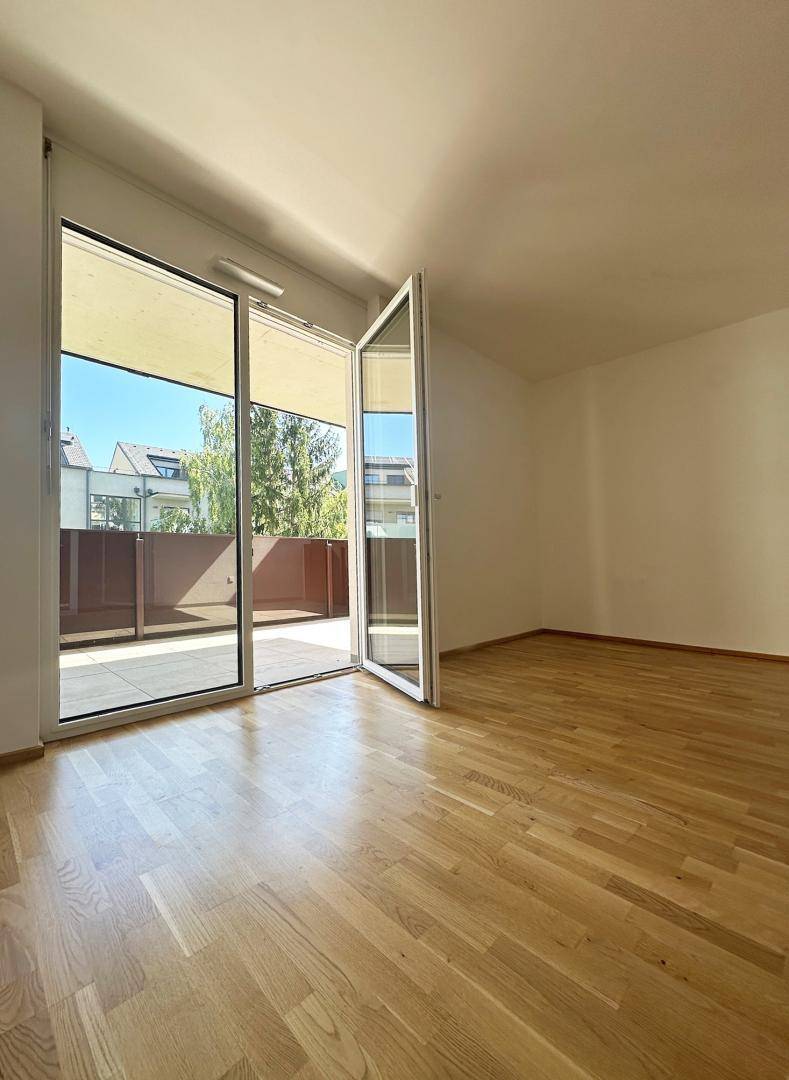 Lichtdurchfluteter Raum mit Holzboden und weit geöffneter Glastür zum sonnigen Außenbereich.