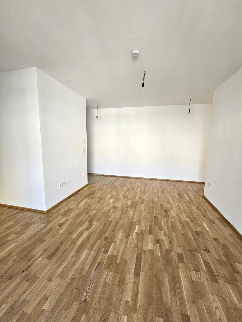 Geräumiger, leerer Raum mit hellem Holzboden und frisch gestrichenen weißen Wänden.