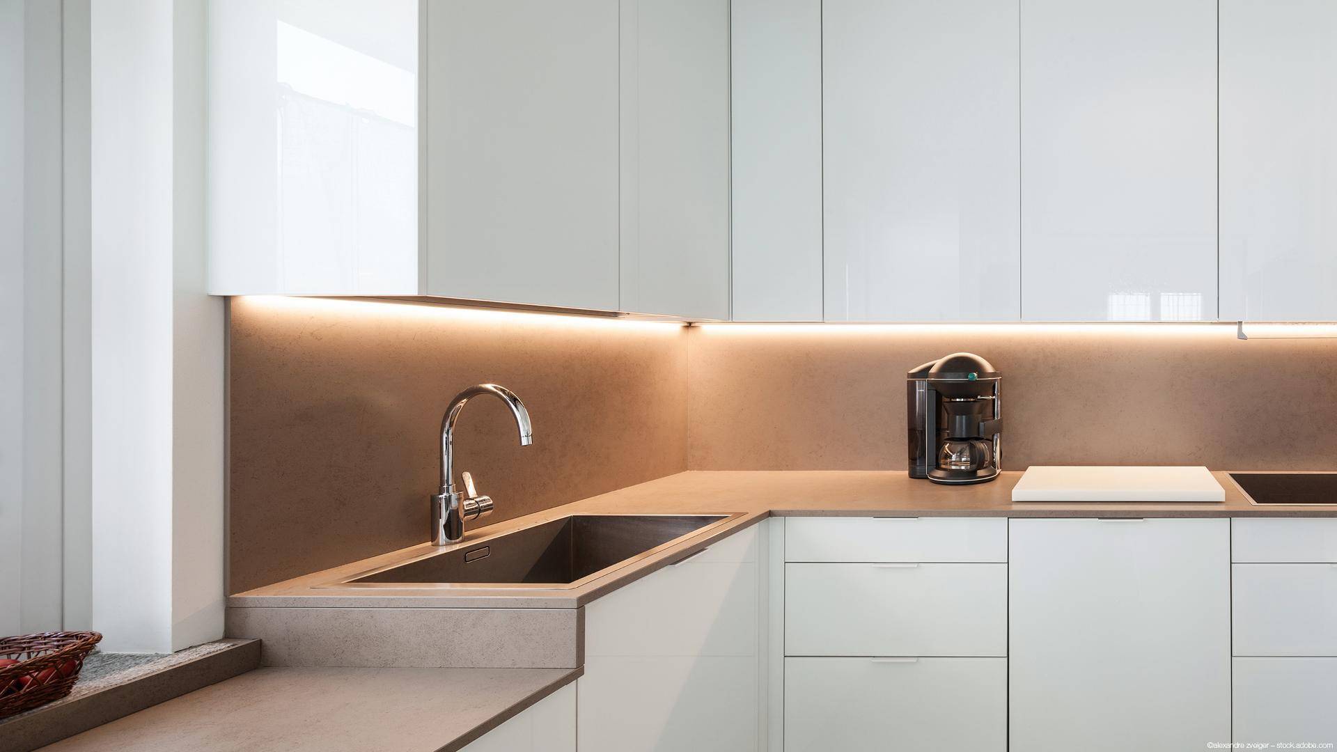 Moderne Küche mit weißen Hochglanzschränken, integrierter Beleuchtung und Spülbecken.