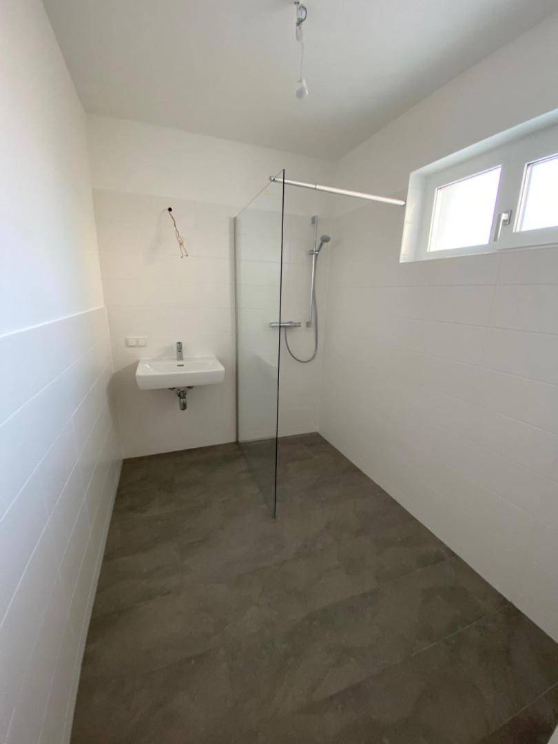 Helles Badezimmer mit modernen Fliesen, ebenerdiger Dusche und Fenster für Tageslicht.