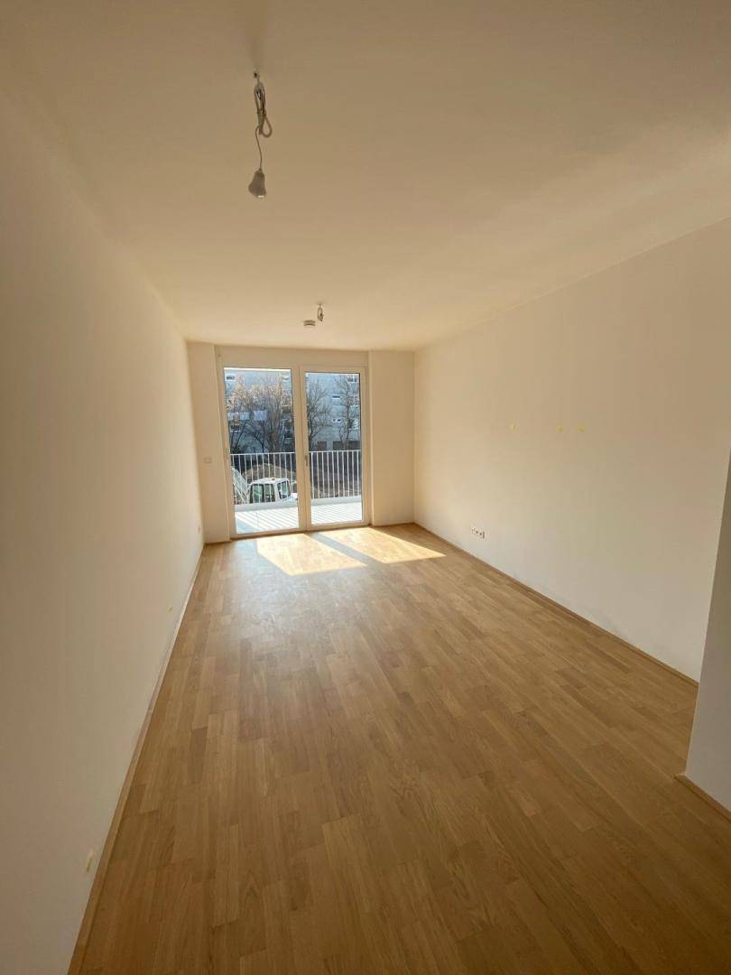 Heller, leerer Raum mit Parkettboden und Zugang zu einem Balkon.