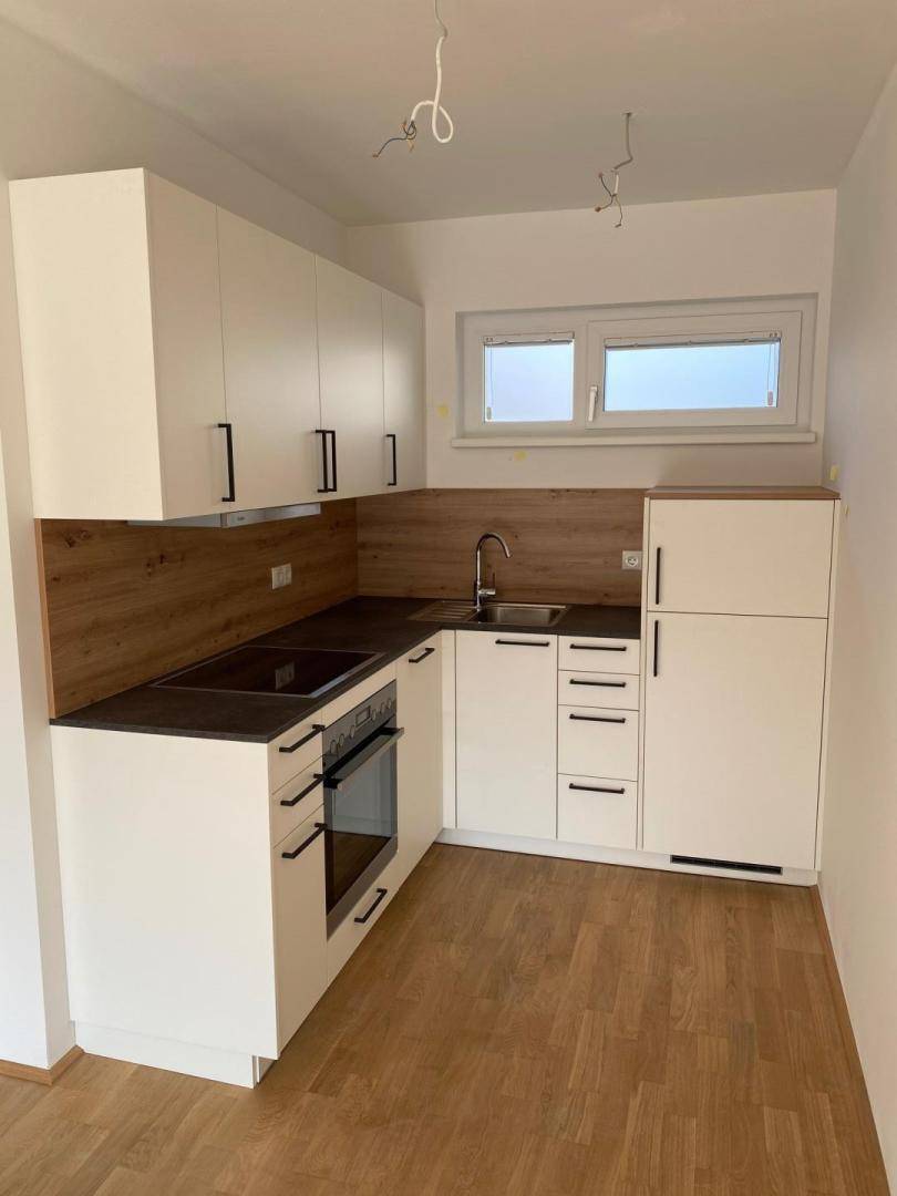 Moderne Einbauküche mit weißen Schränken, dunkler Arbeitsplatte und integrierten Geräten.