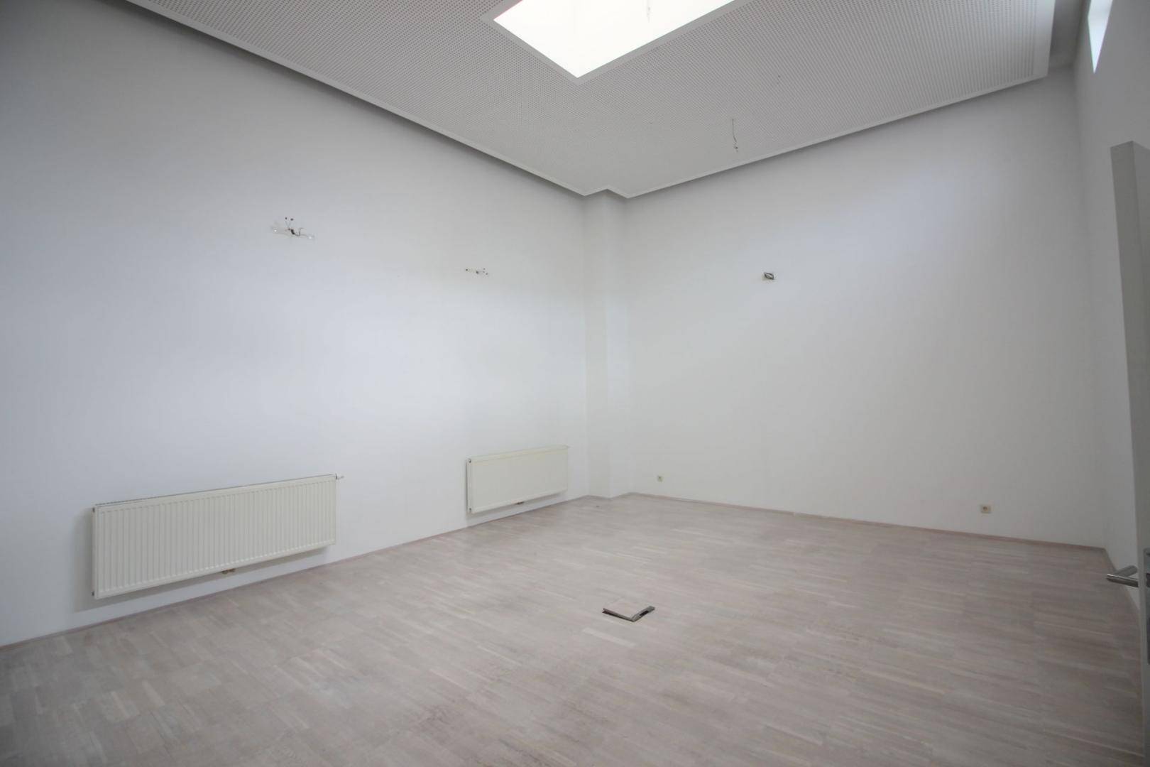 Leerer, heller Büroraum mit Heizkörpern und einem Oberlicht, das für natürliches Licht sorgt.