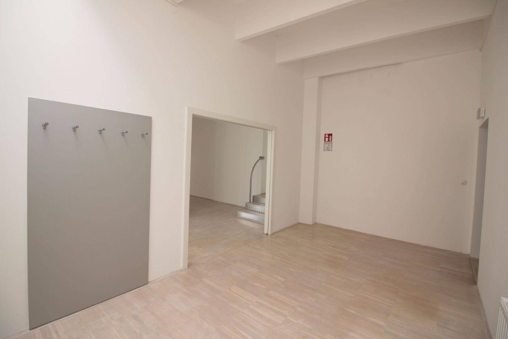 Heller, geräumiger Büroraum mit Garderobenpaneel und Zugang zu einem weiteren Bereich mit Treppe.