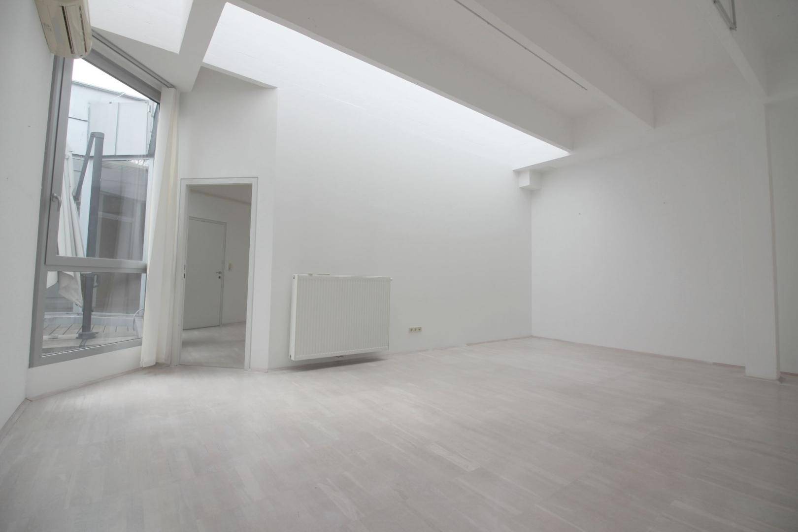 Großer, heller Büroraum mit schrägen Decken, großen Fenstern und Klimaanlage, bietet viel Tageslicht.